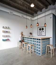 a woman standing in front of a bar with stools and shelves on the wall