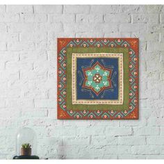 a wall hanging on the side of a white brick wall with an orange and blue rug