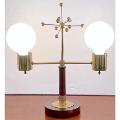 a brass and wood table lamp with two white globes on each arm, sitting on top of a wooden table