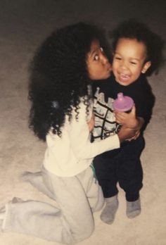 two young children sitting on the ground and one is kissing the other's cheek