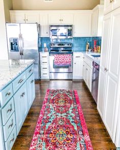 a rug in the middle of a kitchen with white cabinets and blue appliances behind it