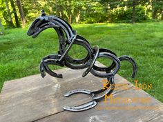 a metal horse sculpture sitting on top of a wooden table in front of some trees