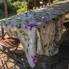 an outdoor table covered with a white floral print cloth and four brown chairs around it