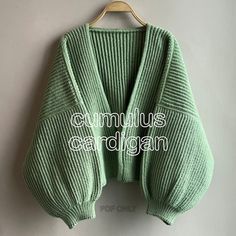 a green cardigan sweater hanging on a wooden hanger with the words cumulus crochet