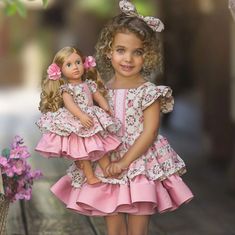 two dolls standing next to each other on a wooden floor with flowers in the background