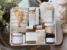 an open box containing various items such as soap, lotion and body wash sitting on a table next to a potted plant