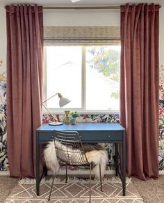 a desk with a chair and lamp in front of a floral wallpapered window