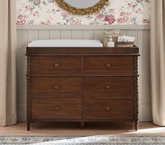 a baby crib in front of a floral wallpapered wall with a mirror above it