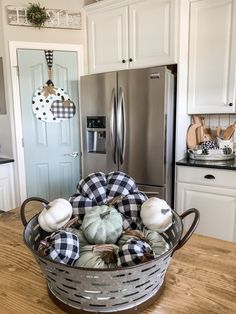 a basket filled with pumpkins sitting on top of a wooden table next to a refrigerator