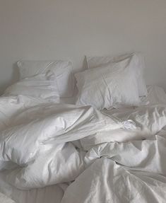 an unmade bed with white sheets and pillows