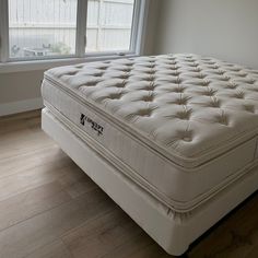 a white mattress sitting in front of a window on top of a hard wood floor