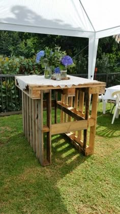 a table made out of wooden pallets in the grass under a white tent with flowers on it