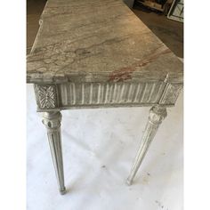 an old table with marble top and metal legs, sitting on a white floor in a room