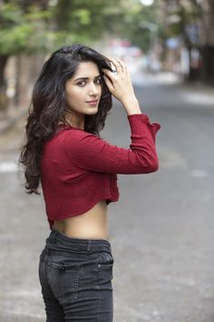 a woman with long hair wearing jeans and a red top is posing for the camera