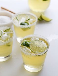 three glasses filled with lemonade and limes on top of a white countertop