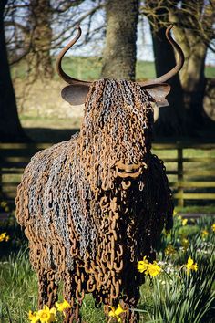 a sculpture of a bull made out of chains in the grass with daffodils around it