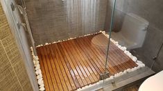 a bathroom with a wooden floor and glass shower door, next to a white toilet