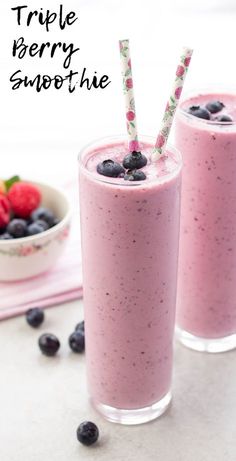 two glasses filled with blueberry smoothie next to berries and strawberries on the table