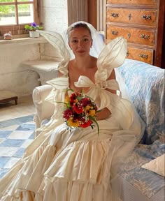 a woman in a wedding dress sitting on a bed holding a bouquet and posing for the camera