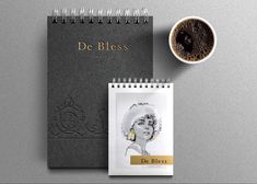 a spiral notebook next to a cup of coffee on top of a gray surface with the words de bless printed on it