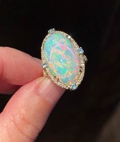 Gorgeous, mesmerizing Ethiopian opal cabochon of AAA quality is framed by dainty diamonds and four blue topazes on each side. The opal sparkles, showcasing streaks and circles of pink, deep blue colors, neon and yellow hues. A truly breathtaking stone! Four soft baby blue round faceted cut topazes add nice detail to the ring. In addition to the frame, diamonds are also placed on the split top part of the band adding more glamour and shine. Very beautiful and elegant ring! Stone: Ethiopian opal, Luxury Adjustable Opal Ring Gift, Luxury Ethiopian Opal Engagement Ring, Luxury Cabochon Opal Ring For Engagement, Luxury Handmade Yellow Gold Opal Ring, Luxury Gold Opal Ring With Diamond Accents, Luxury Adjustable Opal Ring As Gift, Big Opal Ring, Luxury Oval Cabochon Opal Ring For Formal Occasions, Elegant Ethiopian Opal Ring With Oval Cabochon