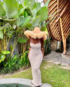 a woman wearing a straw hat standing in front of a pool with plants and greenery