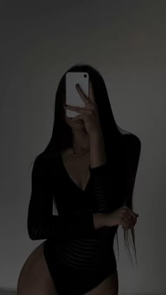 a woman in a black bodysuit taking a selfie with her cell phone while sitting on a bed