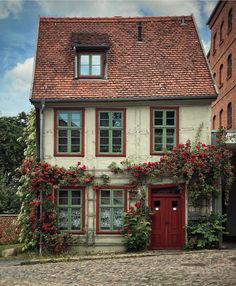 an old house with red flowers growing on it's windows and doors, along with brick buildings