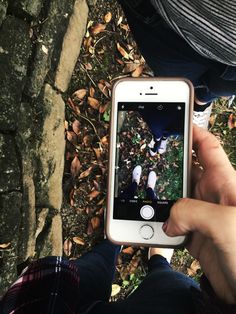 a person holding an iphone in their hand while standing on the ground with leaves around them