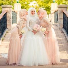 three women in long dresses standing on a bridge with one holding a bouquet and the other wearing hijabs