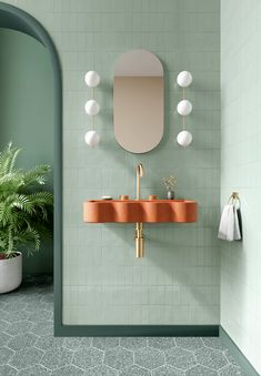 a bathroom with green walls and tile flooring has a sink, mirror, and plant in the corner