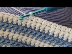 a blue and white crochet stitch being worked on with a green knitting needle