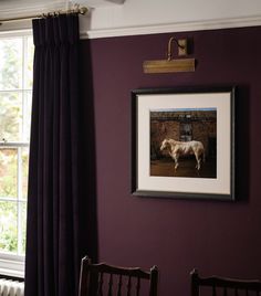 a painting hangs on the wall next to two chairs in front of an open window