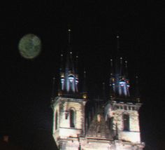 the moon is visible in the dark sky over a building with towers and spires