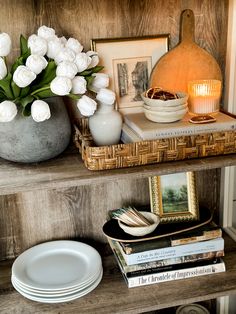 a shelf with books, plates and flowers on it