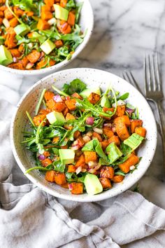 two white bowls filled with salad on top of a marble table next to silverware