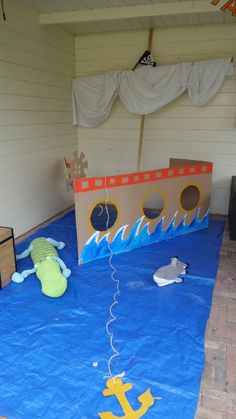 an outdoor play area with cardboard boats and other items on the ground, including a blue tarp