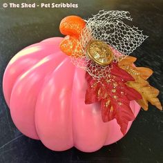 a pink pumpkin sitting on top of a black table next to an orange and yellow leaf