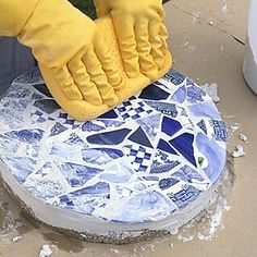 a person in yellow gloves is cleaning a blue and white mosaic tile surface with a rag