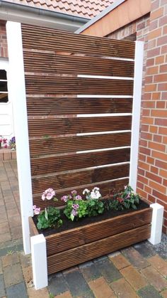 a wooden planter sitting on top of a brick walkway next to a building with flowers growing in it