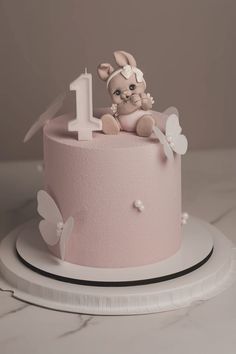 a pink cake decorated with a baby's first birthday candle and bunny on top