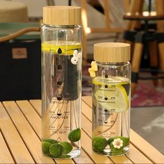 two glass bottles with flowers and leaves in them on top of a wooden table next to each other