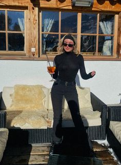 a woman standing in front of a couch holding a drink and posing for the camera