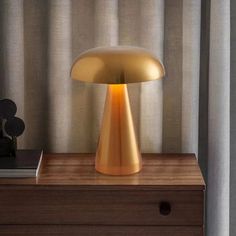 a gold lamp sitting on top of a wooden table next to a window with curtains