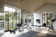 there are many exercise machines in this gym room with large windows and mirrors on the wall