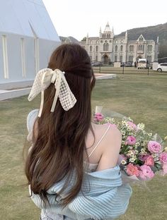 a woman with long hair sitting on the grass in front of some flowers and a building