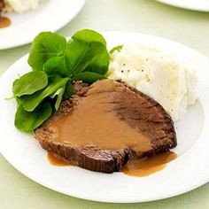 a plate with meat, mashed potatoes and spinach leaves on it next to some gravy