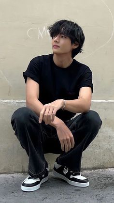 a young man sitting on the ground next to a wall