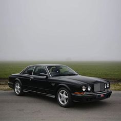 a black car parked on the side of a road in front of a green field