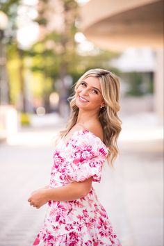 a woman in a pink floral dress posing for a photo with her hand on her hip